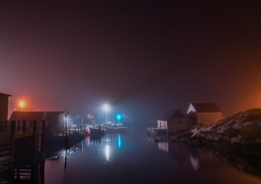 Foggy harbor at night with silhouettes of fishing boats and a lit window