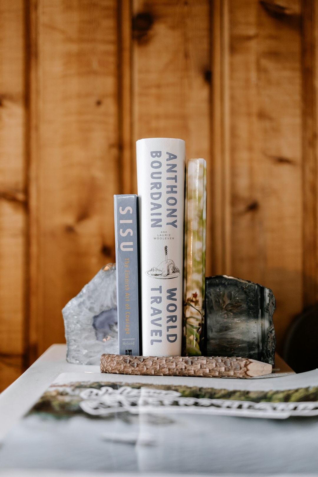 Stack of hardcover mystery novels on a wooden table with a candle and reading glasses